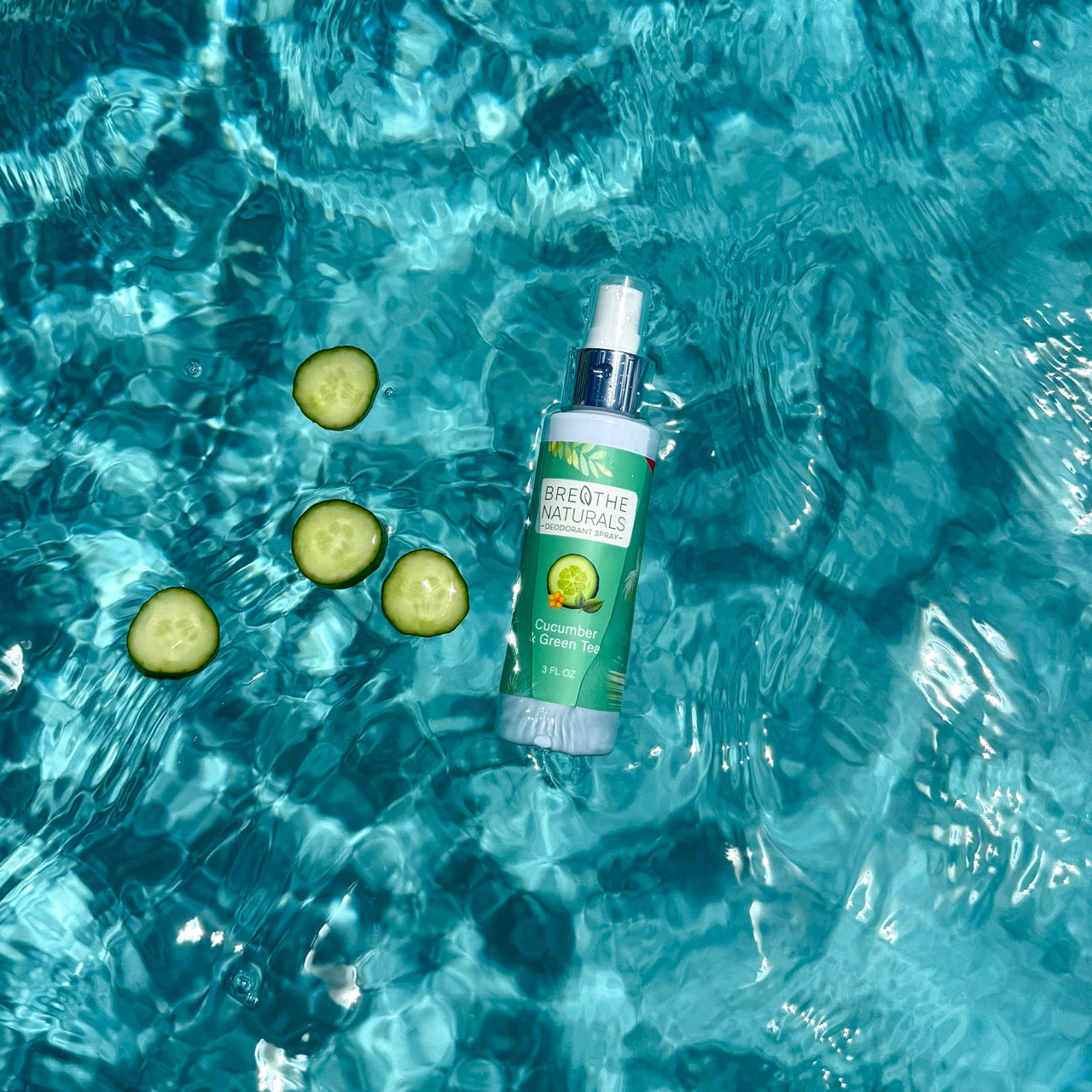 Bottle of 'Breathe The Naturals' cucumber lemonade spray on a blue water background with cucumber slices.