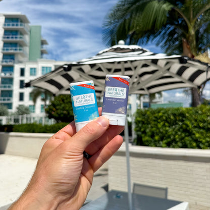 Hand holding two small containers with a scenic background of buildings and trees.