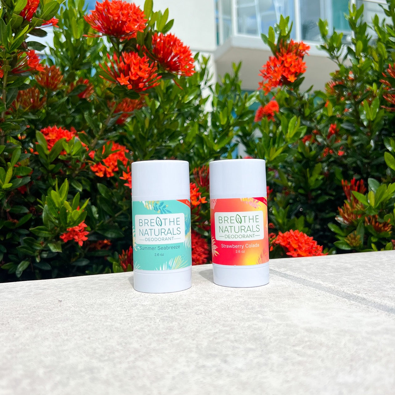 Two Breathe Naturals deodorant sticks on a surface with a floral background