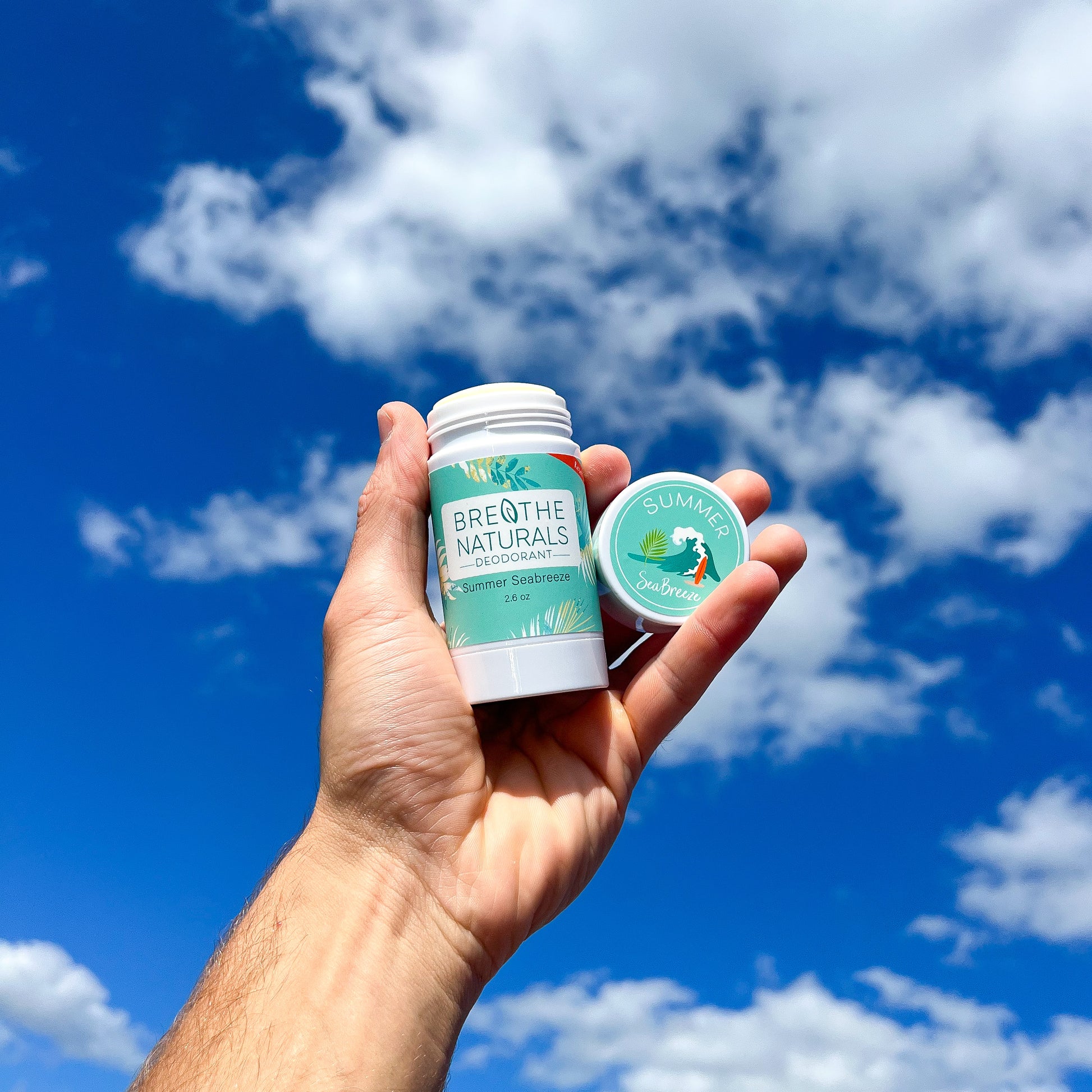 Hand holding two products against a blue sky with clouds